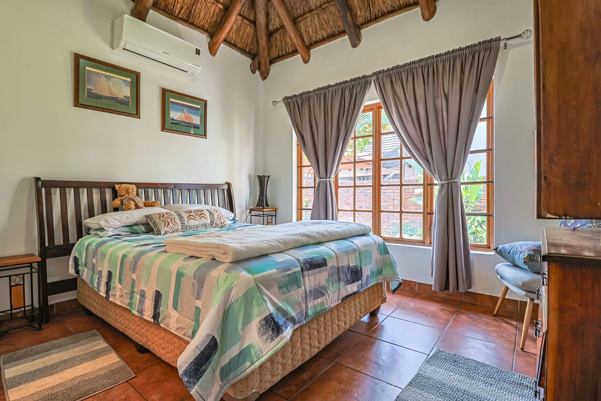 A cozy bedroom featuring a traditional thatched roof with exposed timber rafters, terracotta tiled flooring, and a wall-mounted air conditioning unit.