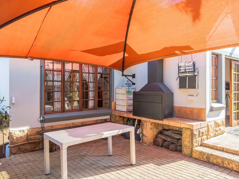 Covered outdoor patio area featuring a built-in braai, stone-clad base, and paved flooring, providing a functional space for outdoor entertaining.