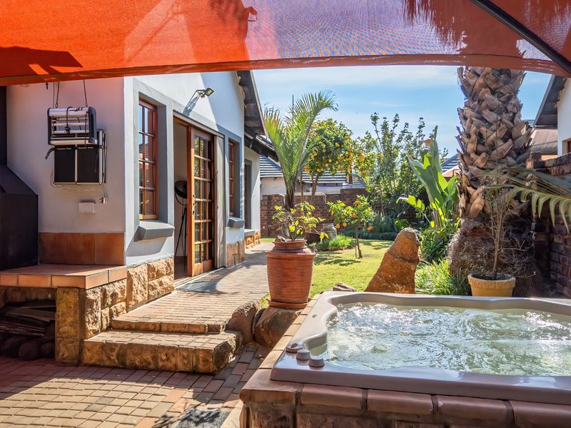 Covered outdoor patio area featuring a built-in braai, a fitted jacuzzi, and direct access to a landscaped garden.