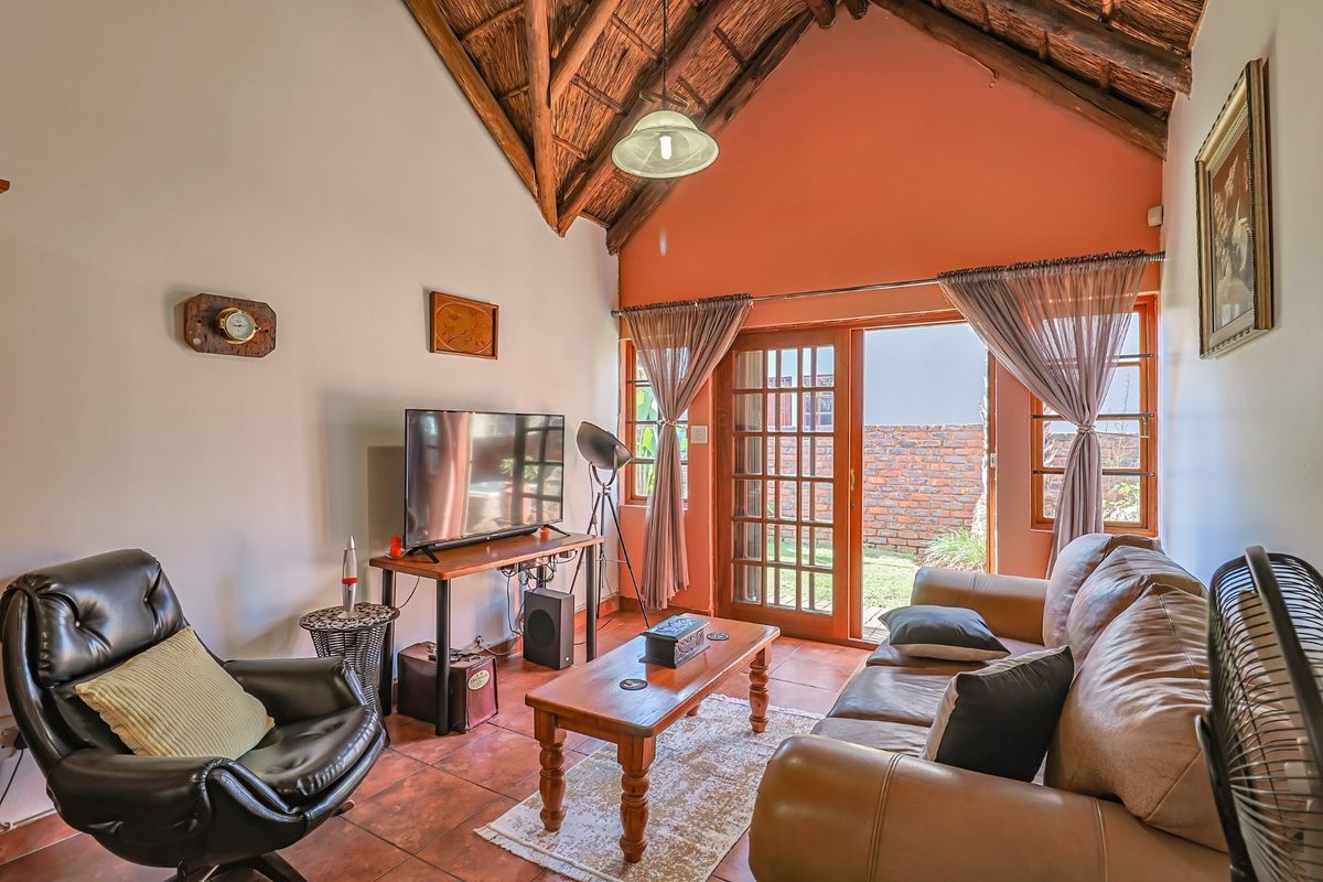 Cozy living room featuring a high vaulted thatched ceiling with exposed timber rafters, terracotta tiled flooring, and direct access to the rear garden.