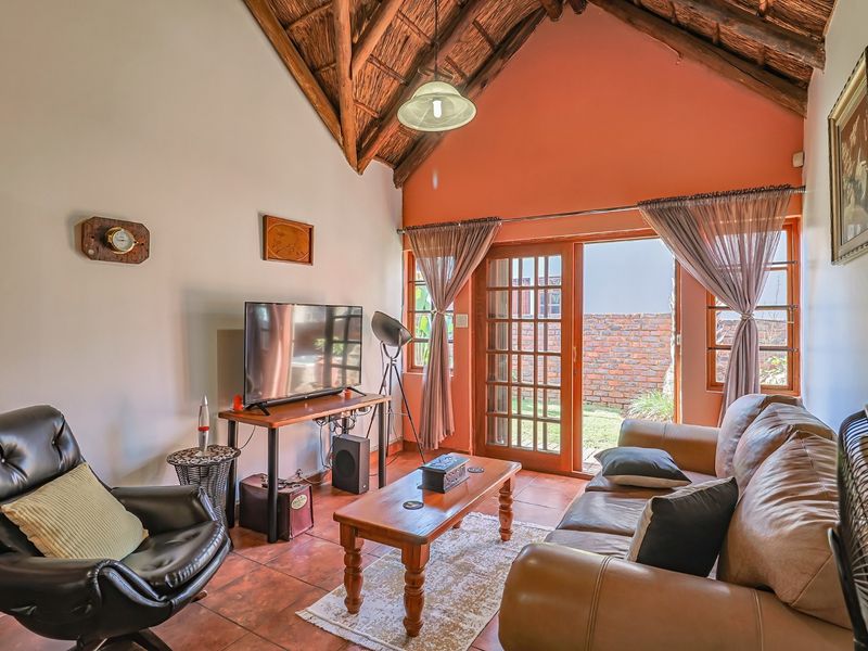 Cozy living room featuring a high vaulted thatched ceiling with exposed timber rafters, terracotta tiled flooring, and direct access to the rear garden.