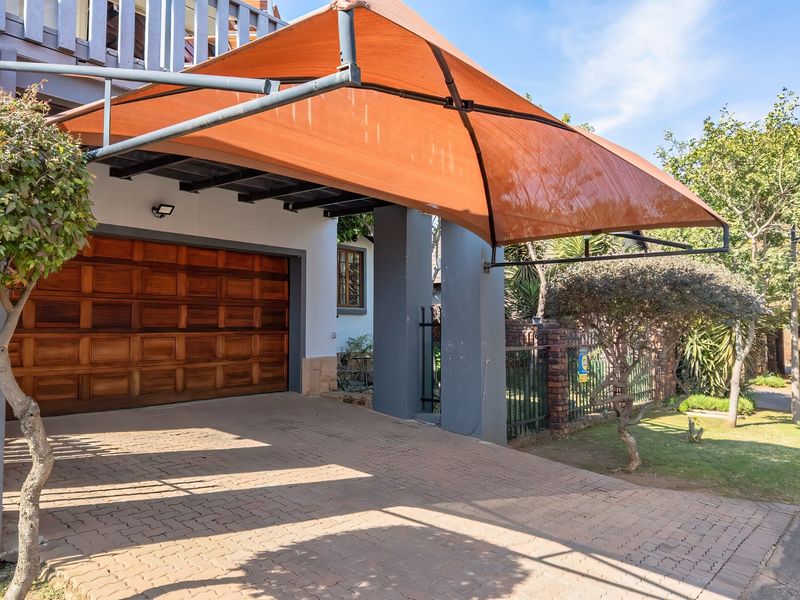 Front exterior view featuring a paved driveway, a timber sectional garage door, and a protective shade sail structure.