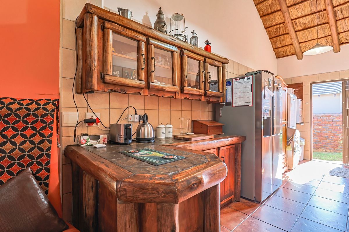 A rustic kitchen featuring custom timber cabinetry, a stone-topped breakfast bar, tiled finishes, and a distinctive high-pitched thatched ceiling.
