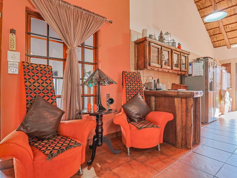 Open-plan living area featuring a high thatched ceiling with exposed rafters, tiled flooring, and rustic timber cabinetry with a breakfast bar.