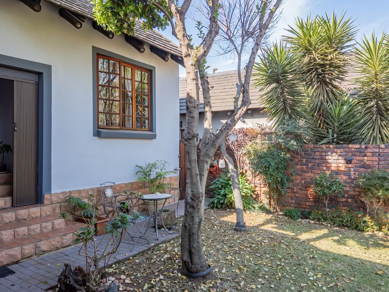 A private rear garden area featuring a paved patio, brick boundary wall, and established trees, providing a quiet outdoor space.