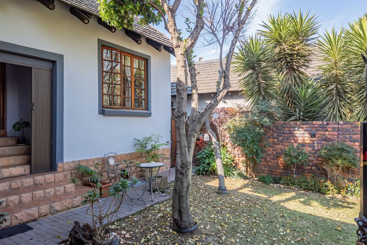 A private rear garden area featuring a paved patio, brick boundary wall, and established trees, providing a quiet outdoor space.
