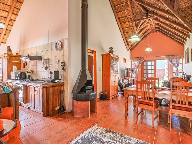 Open-plan living and kitchen area featuring a high thatched ceiling with exposed trusses, tiled floors, and a central freestanding fireplace.