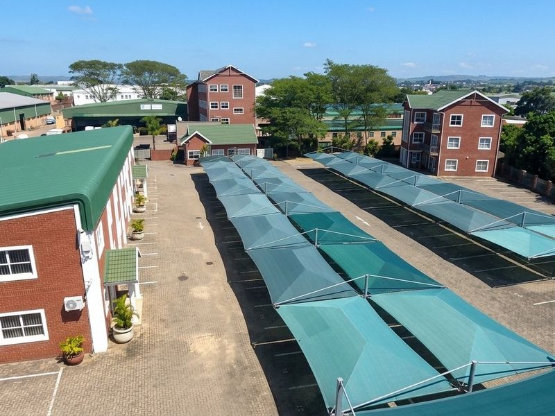 Aerial view of an office complex featuring multiple brick buildings with green metal roofs and an extensive paved parking area with shade cloth carports.