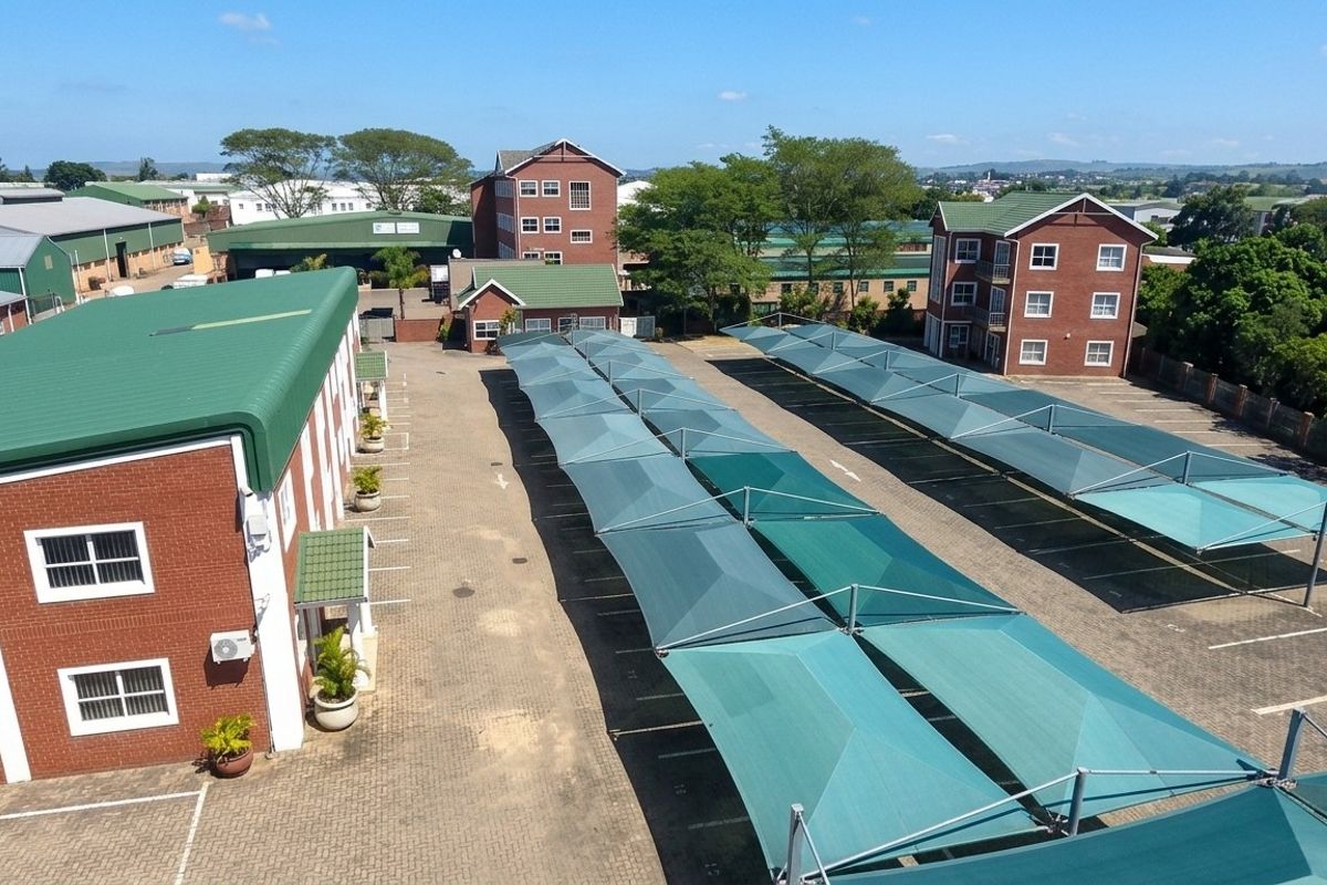 Aerial view of an office complex featuring multiple brick buildings with green metal roofs and an extensive paved parking area with shade cloth carports.