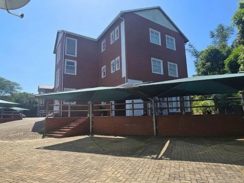 Exterior view of a multi-story brick office building featuring a paved parking area with shade cloth carports and landscaped surroundings.
