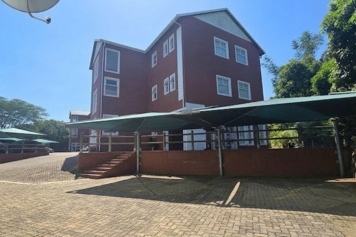 Exterior view of a multi-story brick office building featuring a paved parking area with shade cloth carports and landscaped surroundings.