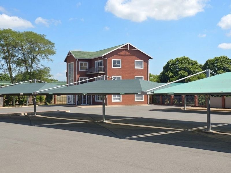 Exterior view of a multi-story brick office building featuring a paved parking area with covered shade cloth carports.