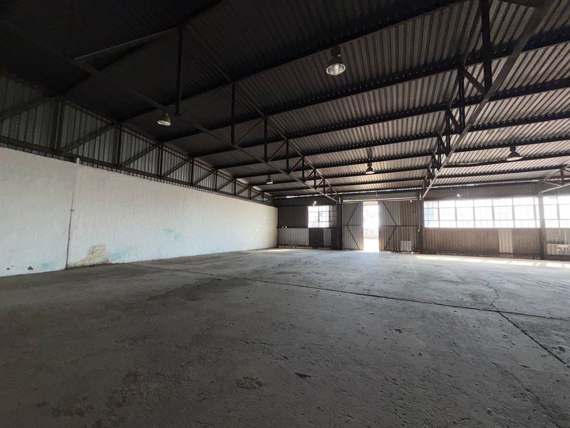 Spacious industrial warehouse featuring high ceilings with exposed steel trusses, concrete flooring, and large sliding doors for easy access.