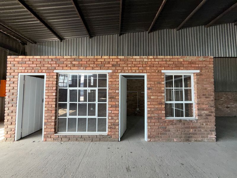An industrial utility space featuring exposed brick walls, steel-framed windows, and a high corrugated metal roof, offering a versatile open-plan layout.