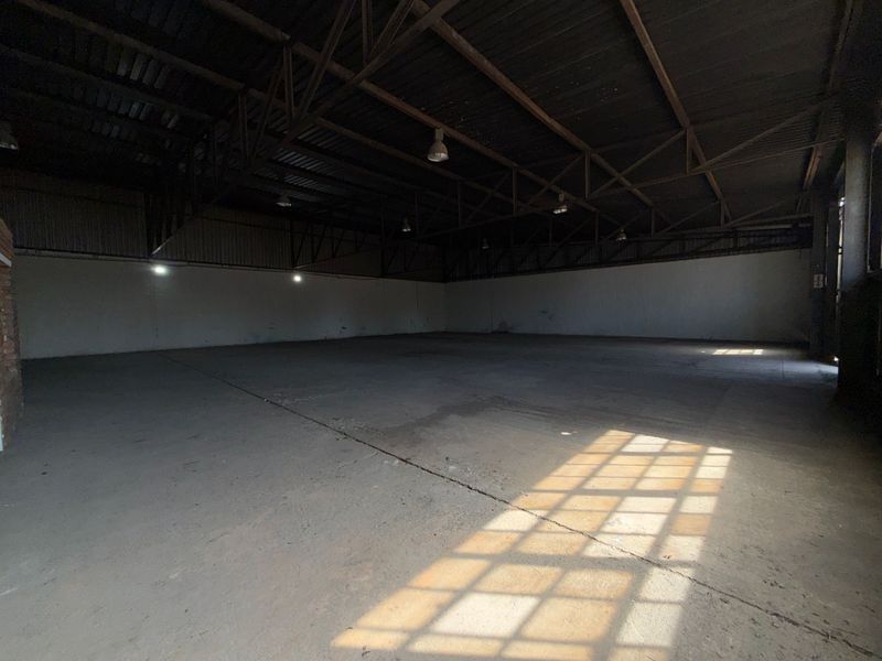 Spacious industrial warehouse unit featuring high exposed steel roof trusses, durable concrete flooring, and functional overhead lighting, suitable for various commercial or storage uses.