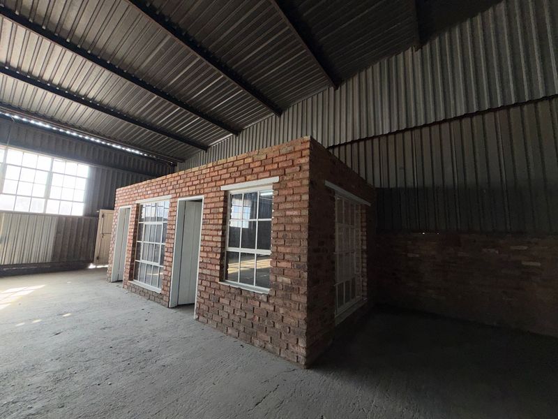 An industrial warehouse space featuring a central face brick structure with steel-framed windows under a high-volume corrugated metal roof.