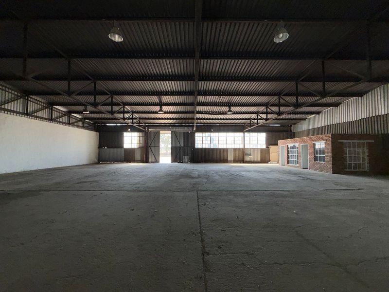 Spacious industrial warehouse featuring high ceilings with exposed steel trusses, concrete flooring, and an integrated brick office structure.