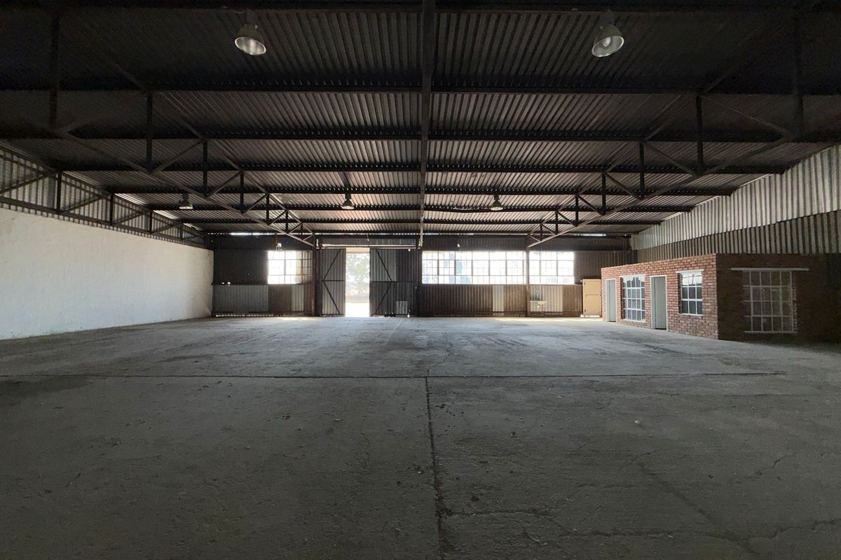 Spacious industrial warehouse featuring high ceilings with exposed steel trusses, concrete flooring, and an integrated brick office structure.