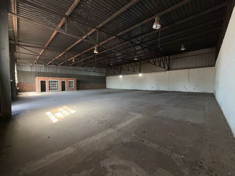 Spacious industrial warehouse featuring high exposed steel roof trusses, concrete flooring, and an integrated brick office structure.