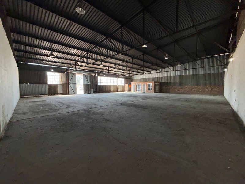 Spacious industrial warehouse featuring high ceilings with exposed steel trusses, concrete flooring, and an integrated brick office structure.