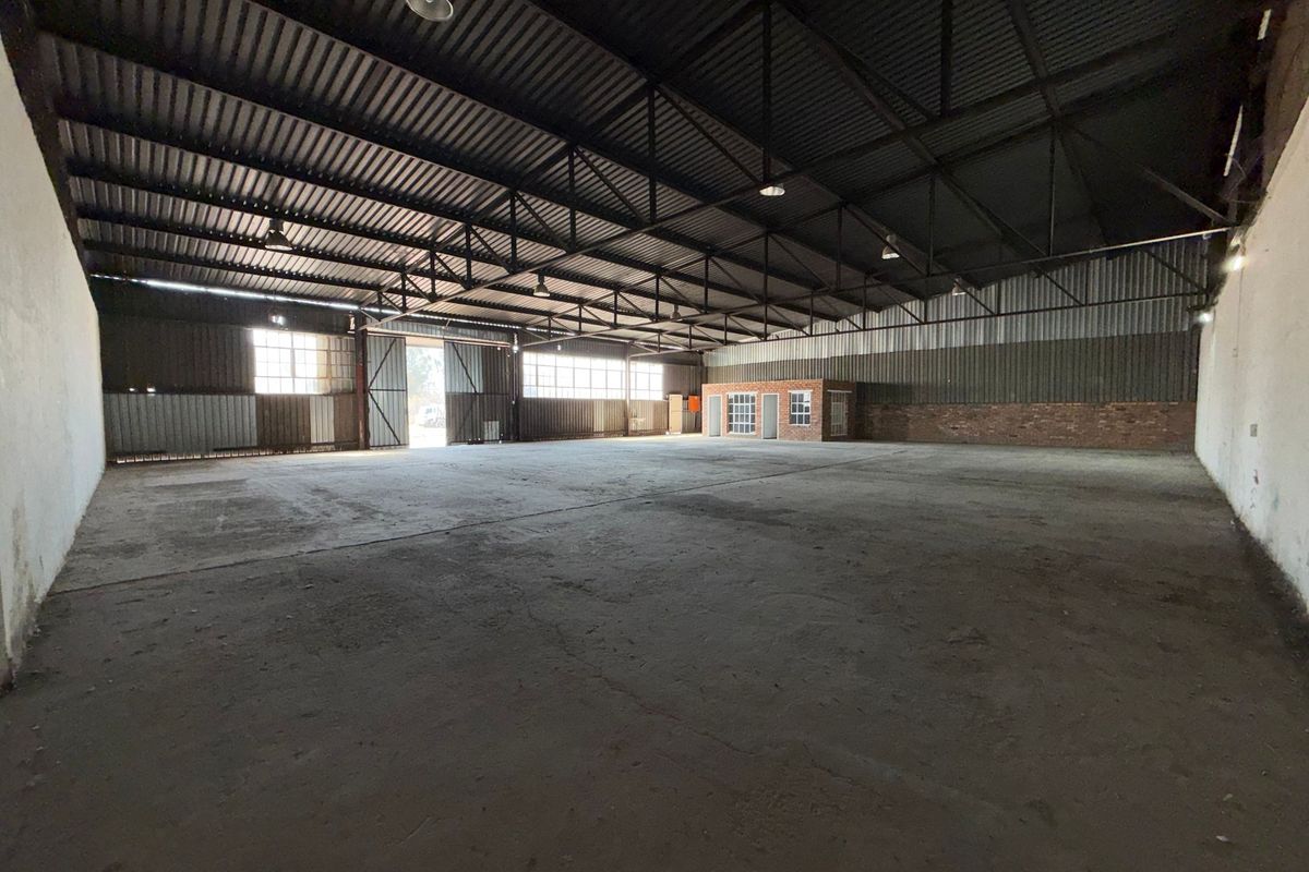Spacious industrial warehouse featuring high ceilings with exposed steel trusses, concrete flooring, and an integrated brick office structure.