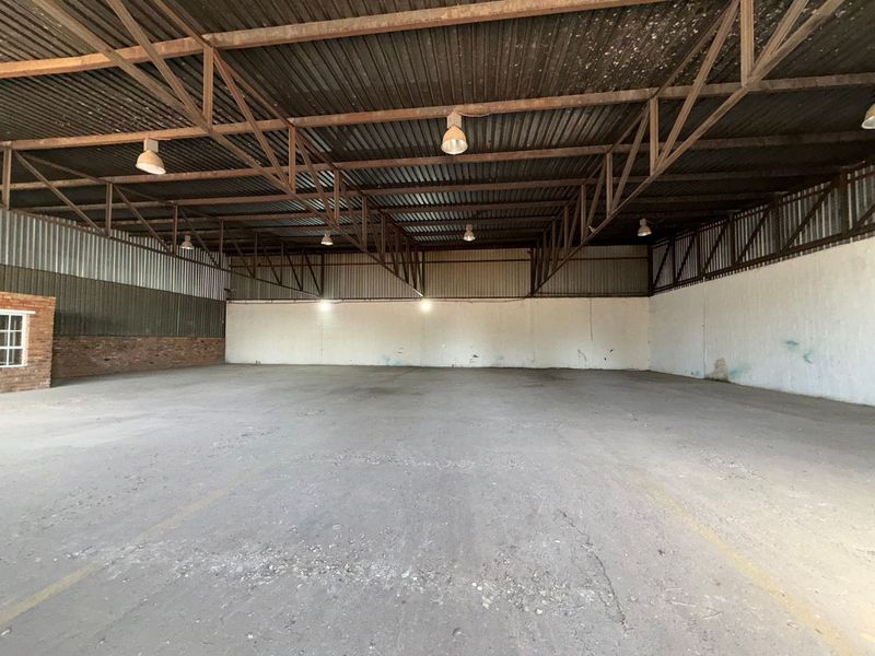 Spacious industrial warehouse unit featuring high ceilings with exposed steel trusses, concrete flooring, and functional industrial lighting throughout.