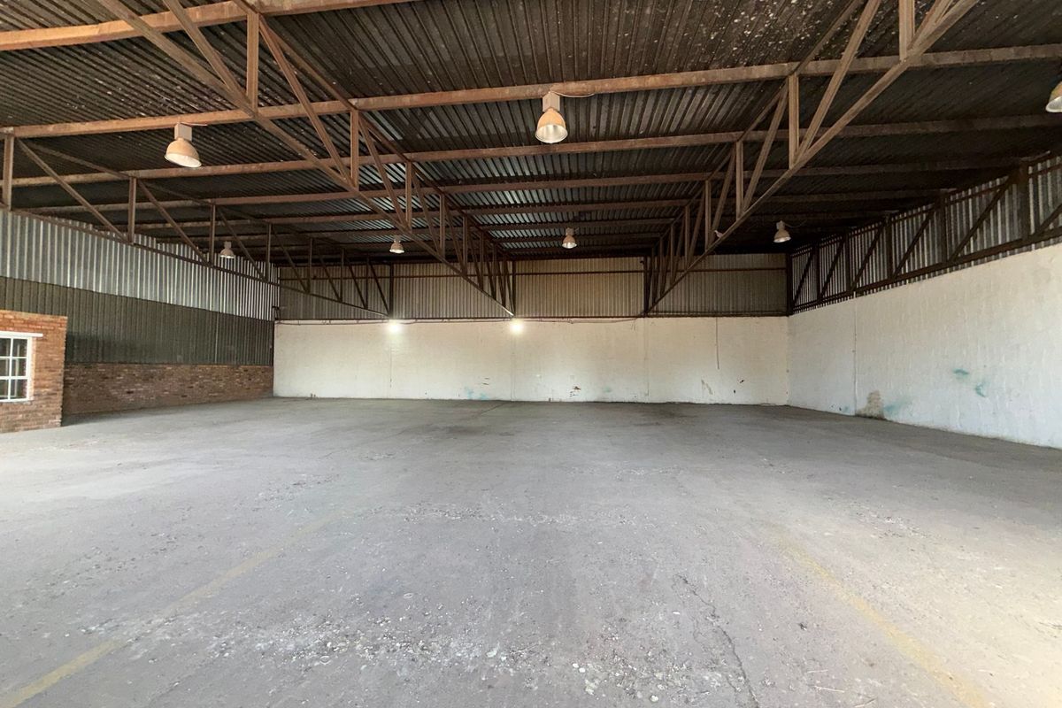 Spacious industrial warehouse unit featuring high ceilings with exposed steel trusses, concrete flooring, and functional industrial lighting throughout.