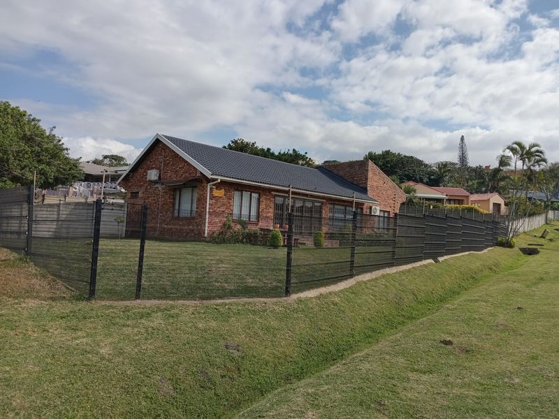 A well-maintained face-brick house featuring a pitched tiled roof, secure perimeter fencing, and a spacious lawn area.