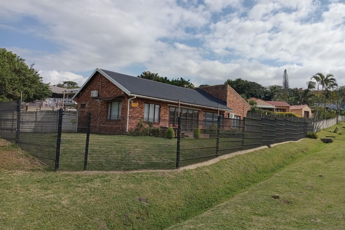 A well-maintained face-brick house featuring a pitched tiled roof, secure perimeter fencing, and a spacious lawn area.