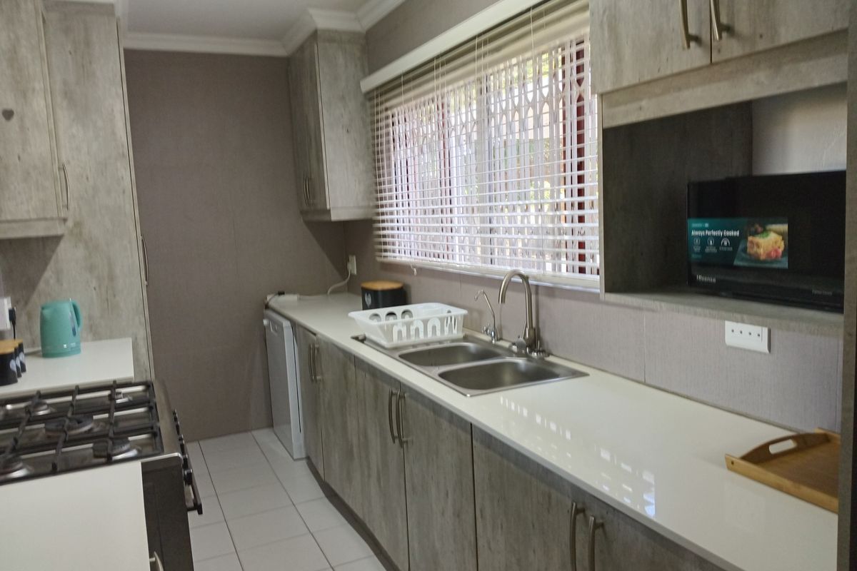 A functional kitchen featuring modern wood-look cabinetry, a gas hob, double basin sink, and ample counter space with tiled flooring.