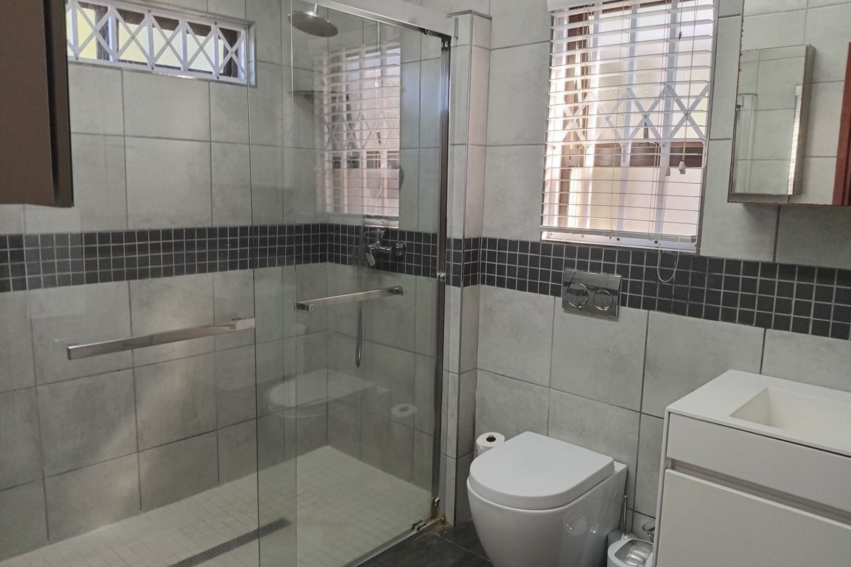 Modern bathroom featuring a spacious walk-in shower with glass enclosure, wall-mounted toilet, and a sleek vanity unit with tiled finishes.