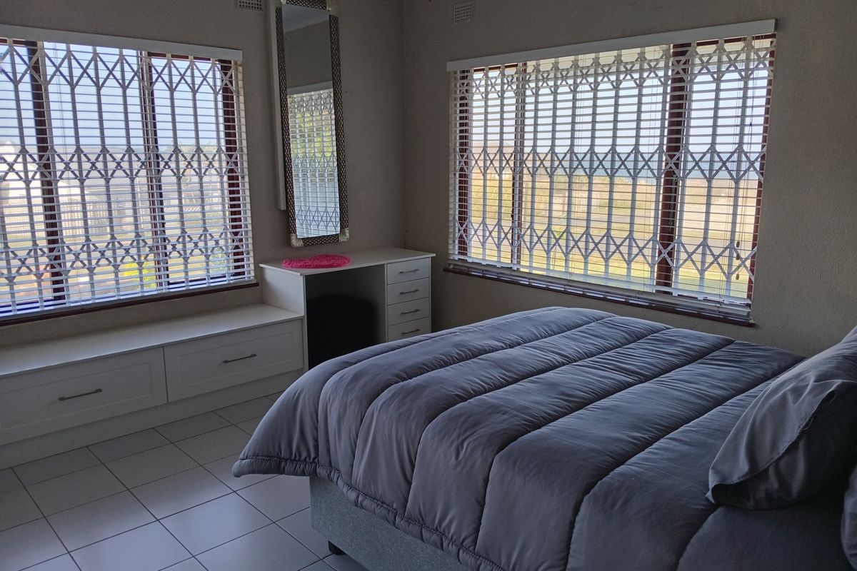 A well-lit bedroom featuring tiled flooring, built-in vanity with storage drawers, and security gates on the windows.