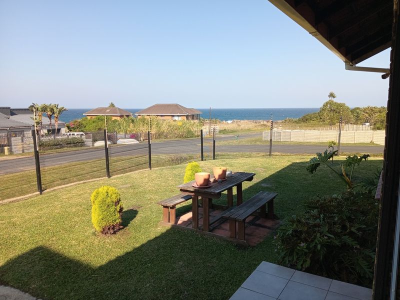 A covered patio area overlooking a private lawn and garden with a clear view of the ocean in the distance.