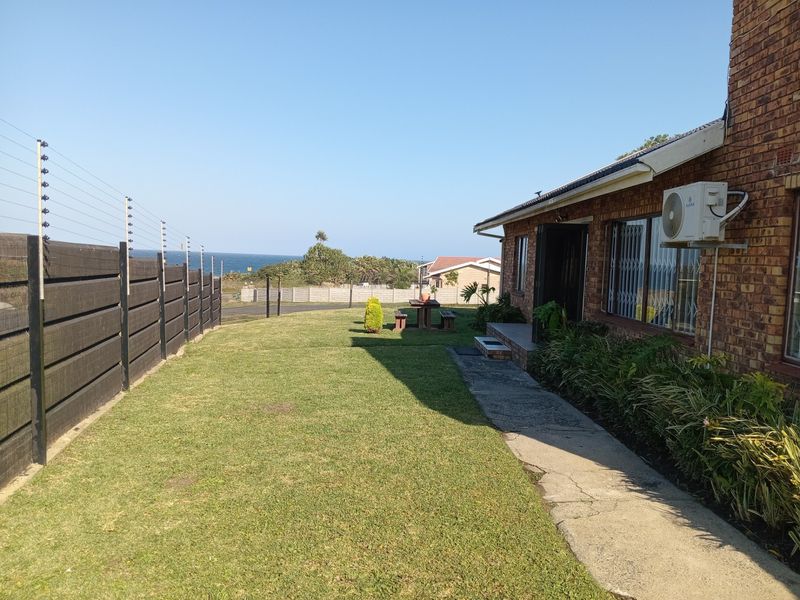 Rear exterior view of the property featuring a brick facade, concrete walkway, and electric fencing with a view towards the ocean.