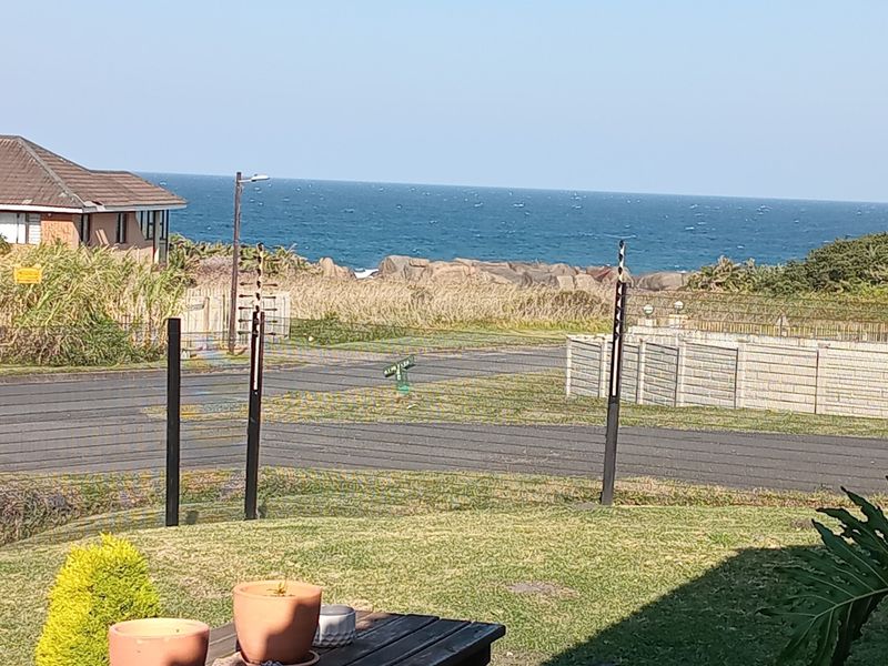 A scenic coastal view overlooking the ocean, featuring a residential street, paved driveway, and secure boundary fencing.