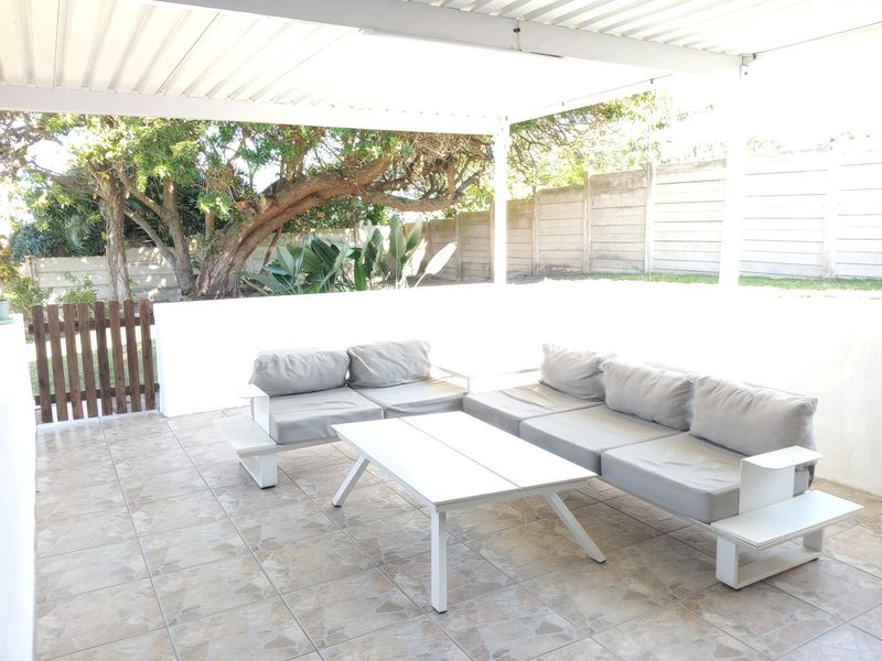A covered outdoor patio area featuring tiled flooring, a low masonry wall, and a timber gate leading to the garden.
