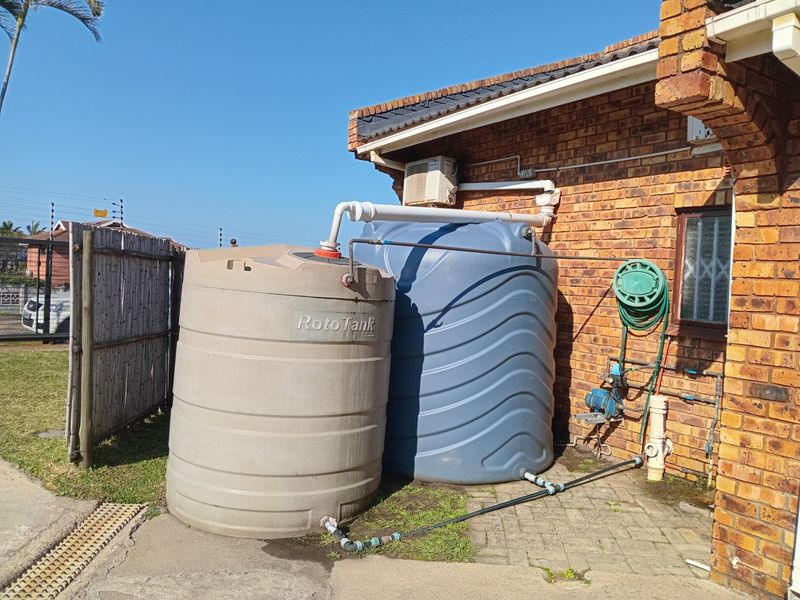 Exterior view of the property featuring two large water storage tanks, a water pump, and brick wall construction.