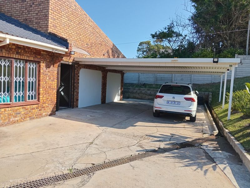 Exterior view of a brick house featuring a covered carport, concrete driveway, and secure entrance access.