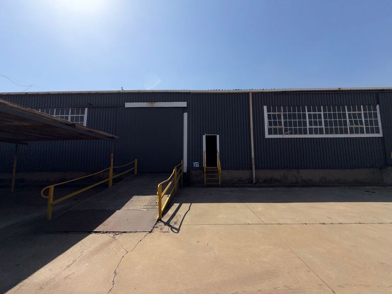 Industrial warehouse exterior featuring a loading ramp, steel-framed windows, and corrugated metal cladding with a concrete apron.
