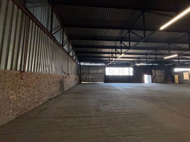 Spacious industrial warehouse featuring high ceilings with exposed steel trusses, concrete flooring, and large sliding access doors, suitable for storage or manufacturing operations.