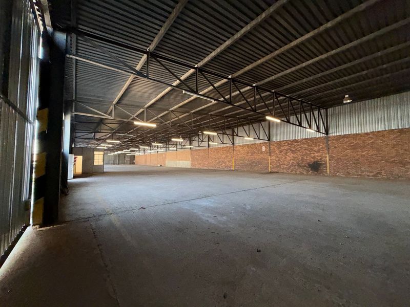 Spacious industrial warehouse featuring high ceilings with exposed steel trusses, durable concrete flooring, and brick wall finishes, suitable for storage or manufacturing operations.