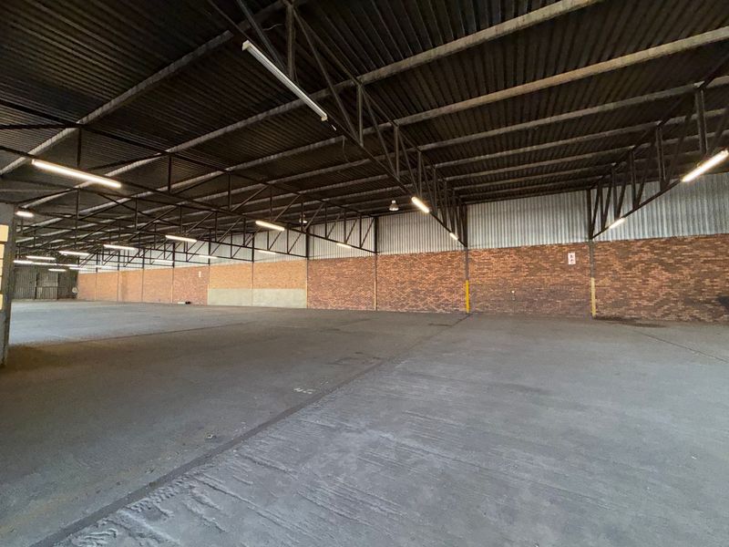 Spacious industrial warehouse unit featuring high ceilings with exposed steel trusses, durable concrete flooring, and brick wall finishes, suitable for storage or manufacturing.