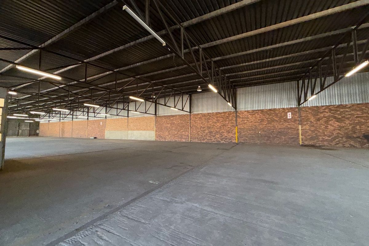 Spacious industrial warehouse unit featuring high ceilings with exposed steel trusses, durable concrete flooring, and brick wall finishes, suitable for storage or manufacturing.
