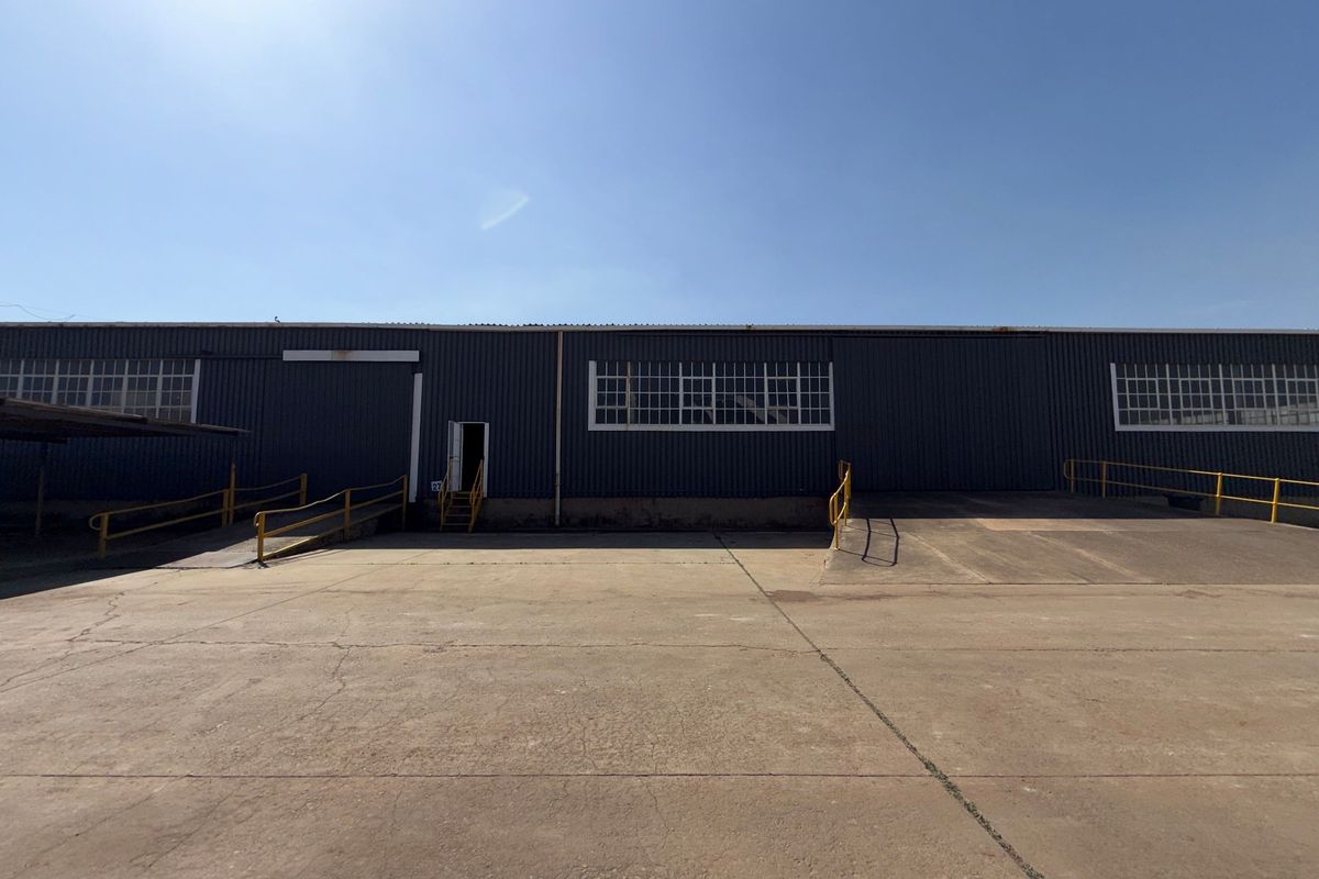 Industrial warehouse exterior featuring a large concrete loading apron, multiple loading ramps with safety railings, and corrugated metal facade with industrial windows.