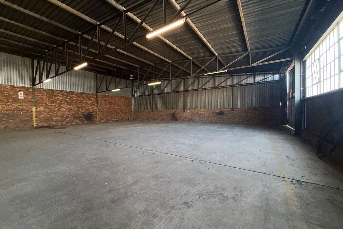 Spacious industrial warehouse unit featuring exposed steel roof trusses, durable concrete flooring, brick wall accents, and ample natural light through large steel-framed windows.