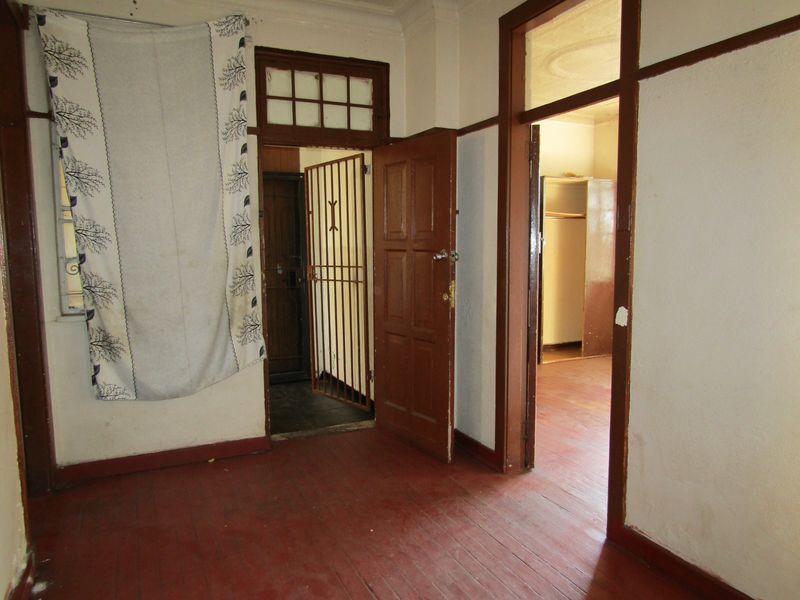 A vacant hallway featuring original timber flooring and wooden door frames, leading to an adjacent room with a built-in cupboard.