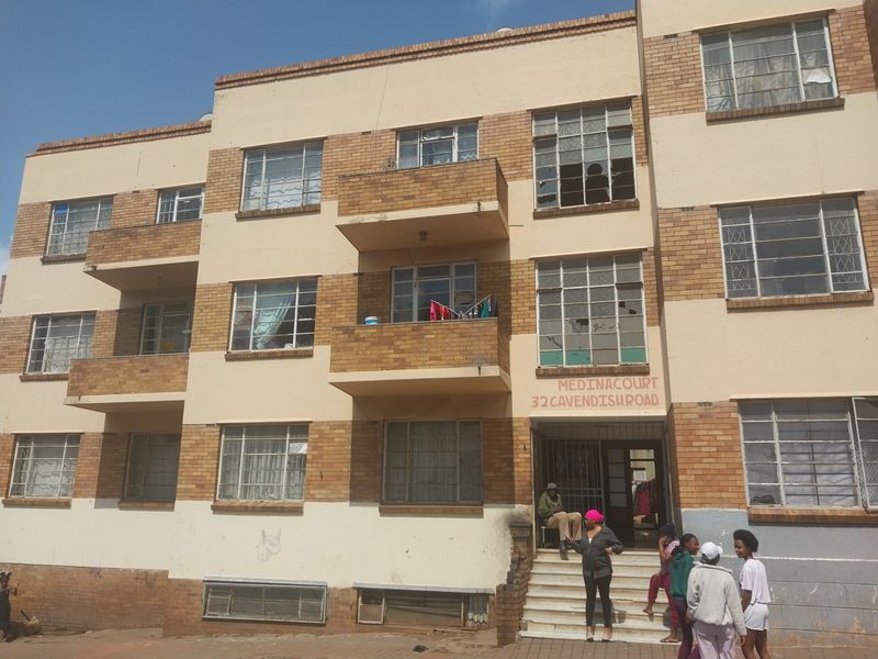 Front elevation of a multi-story apartment building featuring brick and plaster facade, private balconies, and a ground-level entrance staircase.