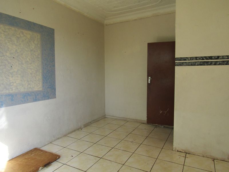An empty bedroom featuring tiled flooring and a simple interior door, requiring cosmetic updates to improve its overall appeal.