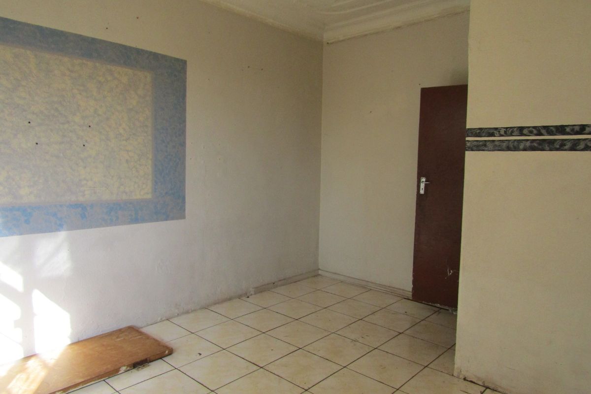 An empty living room featuring ceramic floor tiles, neutral wall finishes, and a standard internal door, ready for renovation or staging.