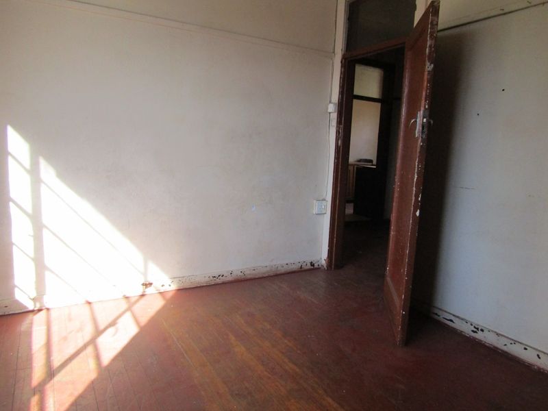 An empty bedroom featuring original timber flooring and a classic timber door, requiring cosmetic updates to restore its character.